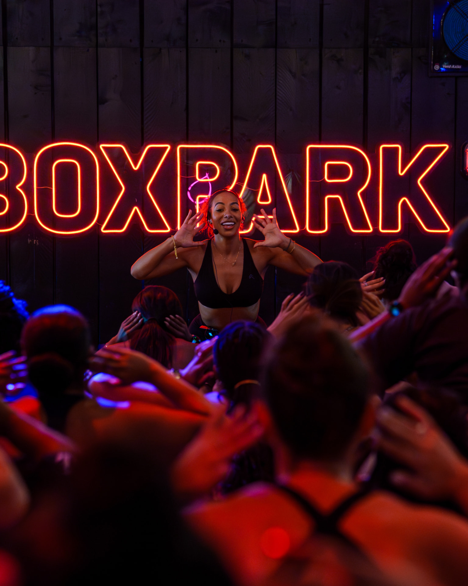 A Bodied By XO instructor leading a class at BOXPARK, attendees raising their arms in front of her